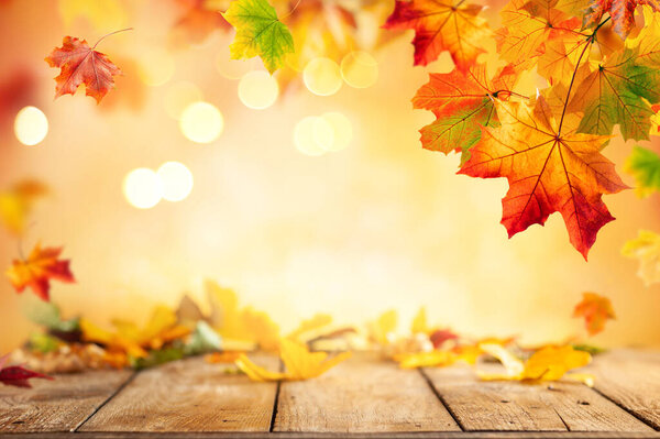 Autumn concept with red-yellow maple leaves. Wooden table and colorful falling leaves over blurred background with boke