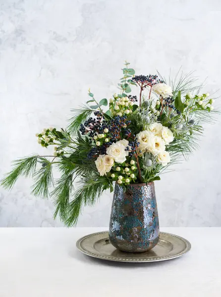 Vazoda güzel bir kış buketi. Güllerle çiçek aranjmanı, köknar dalları, kış meyveleri, okaliptüs ve eryngium. Noel çiçeği süslemesi.