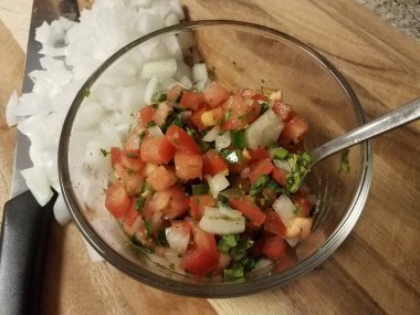 glass bowl of tomato peppers and onion salsa with knife and cutting board