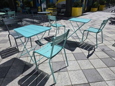Canlı metal sandalyeler ve masalar güneşli bir açık havada canlı ve davetkar bir oturma alanı oluşturuyor..