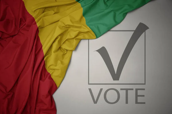 Machanie Kolorową Flagą Narodową Gwinei Szarym Tle Głosowaniem Tekstowym Koncepcja — Zdjęcie stockowe