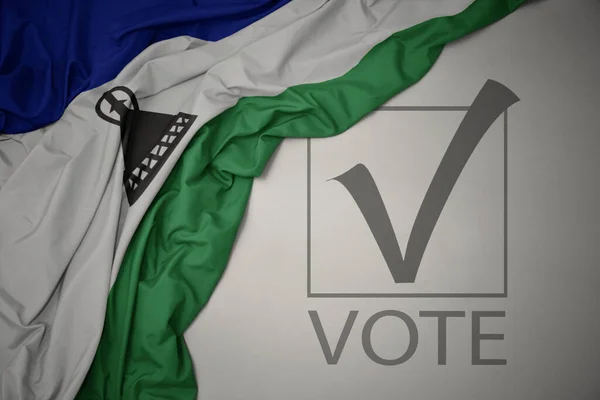 Machanie Kolorową Flagą Narodową Lesotho Szarym Tle Głosowaniem Tekstowym Koncepcja — Zdjęcie stockowe