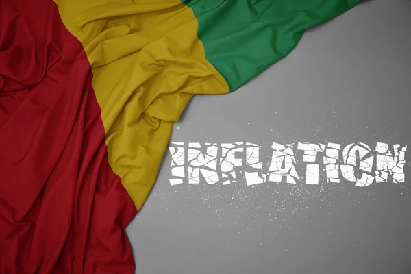 stock image waving colorful national flag of guinea on a gray background with broken text inflation. concept. 3d illustration