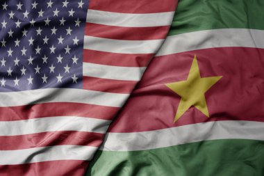 big waving colorful flag of united states of america and national flag of suriname . macro