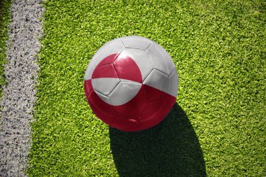 Yeşil bayrağı olan futbol topu beyaz çizginin yanındaki yeşil alanda.