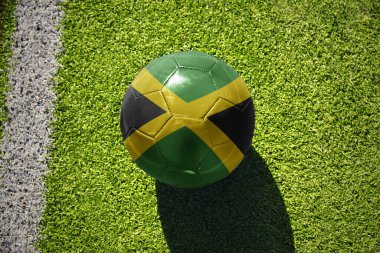 Jamaika milli bayraklı futbol topu beyaz çizginin yanındaki yeşil sahada.