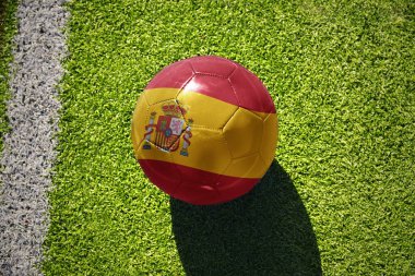 İspanya milli bayraklı futbol topu beyaz çizginin yanındaki yeşil sahada.