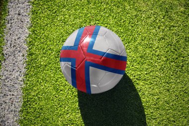Faraday adalarının ulusal bayrağını taşıyan futbol topu beyaz çizginin yanındaki yeşil alanda.