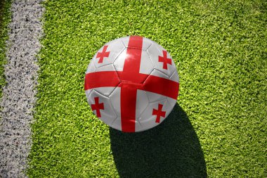 Gürcistan 'ın ulusal bayrağını taşıyan futbol topu, beyaz çizginin yanındaki yeşil alanda.