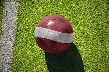 Beyaz çizginin yanındaki yeşil alanda ulusal Letonya bayrağı taşıyan futbol topu.