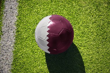 Beyaz çizginin yanındaki yeşil alanda ulusal Katar bayrağı taşıyan futbol topu.