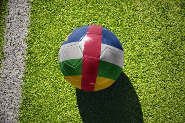 Orta Afrika Cumhuriyeti 'nin ulusal bayrağını taşıyan futbol topu beyaz çizginin yanındaki yeşil alanda.