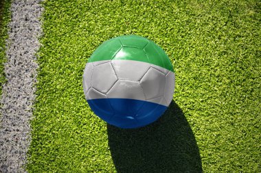 Sierra Leone 'nin ulusal bayrağını taşıyan futbol topu beyaz çizginin yanındaki yeşil alanda.