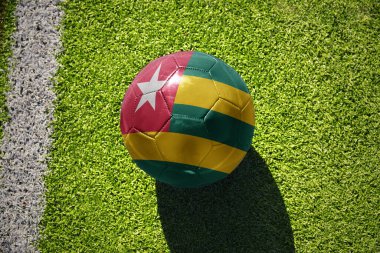 Beyaz çizginin yanındaki yeşil alanda ulusal togo bayrağı taşıyan futbol topu.