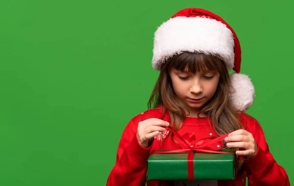 Een Schattig Klein Meisje Met Een Kerstmuts Pakt Een Nieuwjaarscadeau — Stockfoto