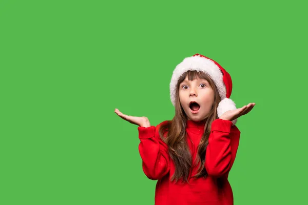 戴圣诞老人帽的女孩吃惊地张开嘴 双手朝不同方向 除夕夜和圣诞节有什么折扣 促销和礼物呢 儿童的情感画像 — 图库照片