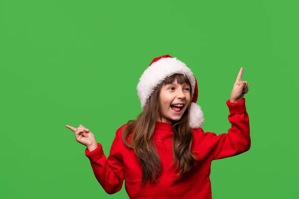一个戴着圣诞礼帽的笑容满面的女孩带着食指打折 促销和礼物 在绿色背景下孤立的情感肖像 新年和圣诞节的概念 高质量的照片 — 图库照片