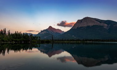 Kanada Alberta 'daki Gap Gölü, günbatımından sonra sakin sulardaki çarpıcı yansıma dağları ve renkli gökyüzünü yansıtıyor.