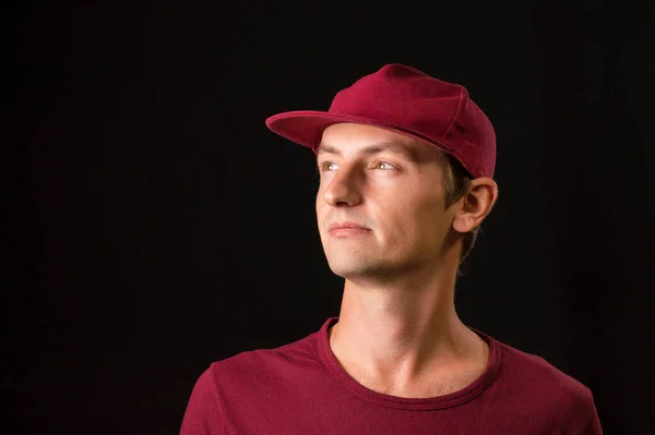 man on a black background in a burgundy cap and t-shirt