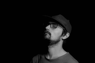 Gözlüklü ve siyah arka planda şapkası olan bir adamın portresi.