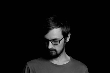 Siyah arka planda gözlüklü sakallı bir adamın portresi.