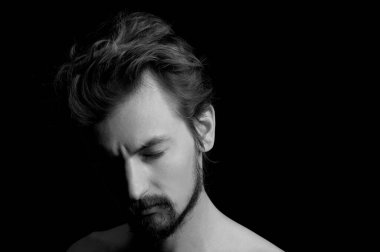 Siyah arka planda sakallı ve dağınık saçlı bir adamın portresi.