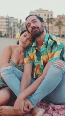 Kumsalda battaniyenin üzerinde oturup sarılan mutlu çift.