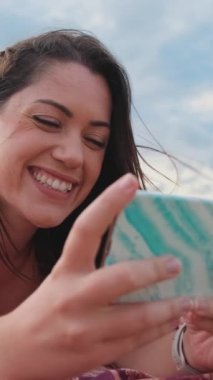 Yakından bakınca, genç bayan kumsalda dinlenirken akıllı telefon kullanıyormuş gibi görünüyor. Kız başını kaldırır ve kameraya bakıp gülümser.