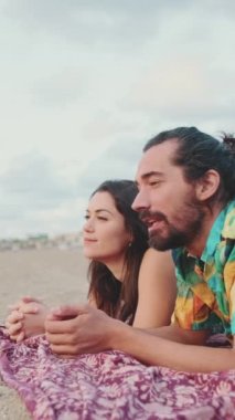 Kadın ve erkek sahilde battaniyede konuşuyor ve dinleniyorlar.