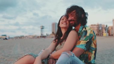 Kadın ve erkek kumsalda birbirlerine sarılıp şafağı izliyorlar.