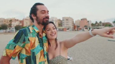 Yeni evliler sahilde dikilirken sarılıp konuşurlar.