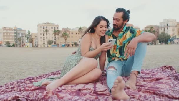 Молодая Пара Использует Мобильный Телефон Сидя Пляже Фоне Зданий — стоковое видео