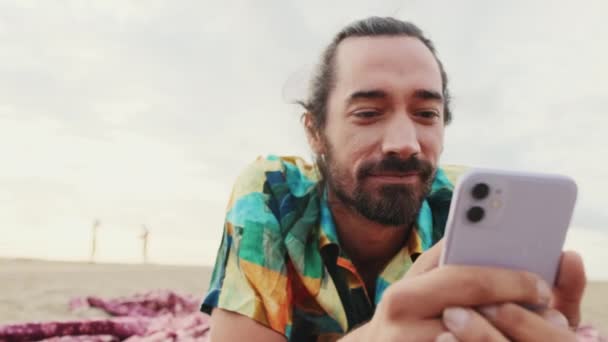 靠近点 微笑着的男人手里拿着智能手机在海滩上放松 — 图库视频影像