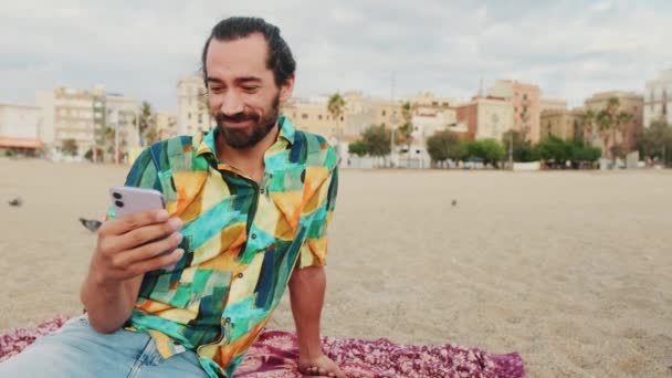 Νεαρός Χαρούμενος Άντρας Που Χρησιμοποιεί Κινητό Τηλέφωνο Στην Παραλία — Αρχείο Βίντεο