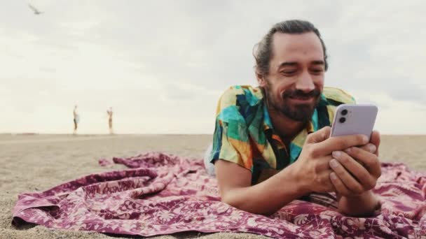 Homme Souriant Relaxant Sur Plage Avec Smartphone Dans Les Mains — Video