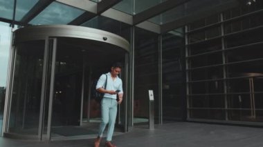 Genç işadamı akıllı telefonuyla iş merkezinden ayrılıyor.