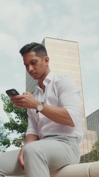 Vertical Video Młody Biznesmen Korzystający Telefonu Komórkowego Siedząc Obok Centrum — Wideo stockowe