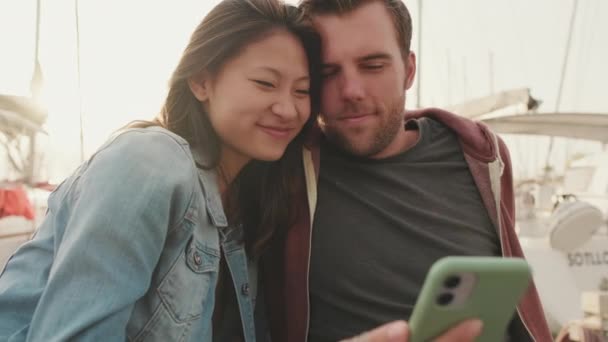 桟橋に座っている間に携帯電話を使用して若いカップル — ストック動画