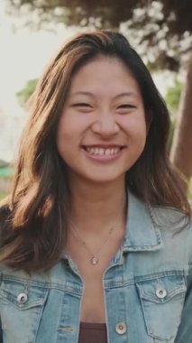 Parkta dikilirken kameraya poz veren gülen genç kadın.