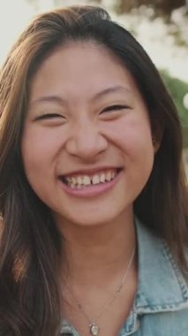 Yakın çekim, parkta dururken kameraya poz veren gülen genç kadın.