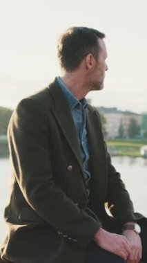 Adam nehrin arka planındaki toprak setinde otururken etrafına bakınır.