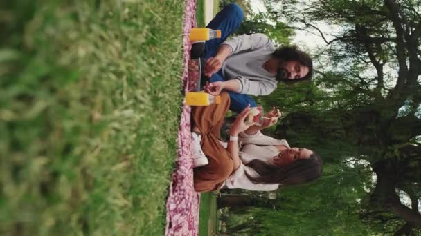 Vertical Video 男人和女人在户外野餐时坐在毛毯上吃着健康的午餐 — 图库视频影像