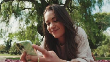 Parkta tatilden zevk alan ve cep telefonu kullanan genç bir kadının yakın çekimi.