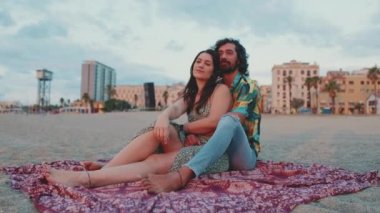 Erkek ve kadın sahilde sarılıp öpüşüyor ve şafağı seyrediyor.