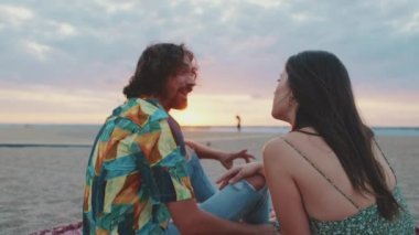 Erkek ve kadın gün doğumunda sahilde birbirleriyle konuşuyorlar.