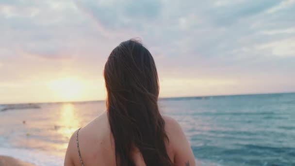 若い女性はビーチで日の出を見て立っている バックビュー — ストック動画