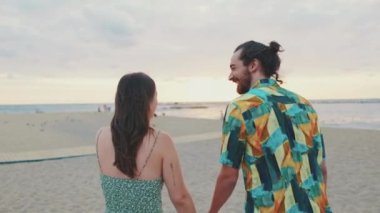 Erkek ve kadın gün doğumunda kumsalda durup birbirleriyle konuşuyor ve gülüyorlar.