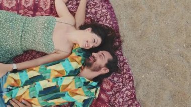 Kumsalda battaniyenin üzerinde yatarken birbirlerinin iletişiminden zevk alan mutlu bir çift. Üst görünüm