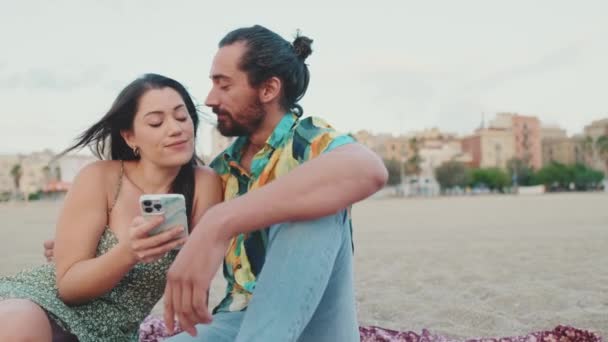 Romantic Couple Uses Mobile Phone While Sitting Beach Buildings Background — Stock Video