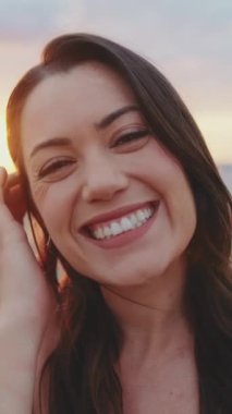 Kumsalda dikilirken kameraya gülümseyen genç bir kadın.